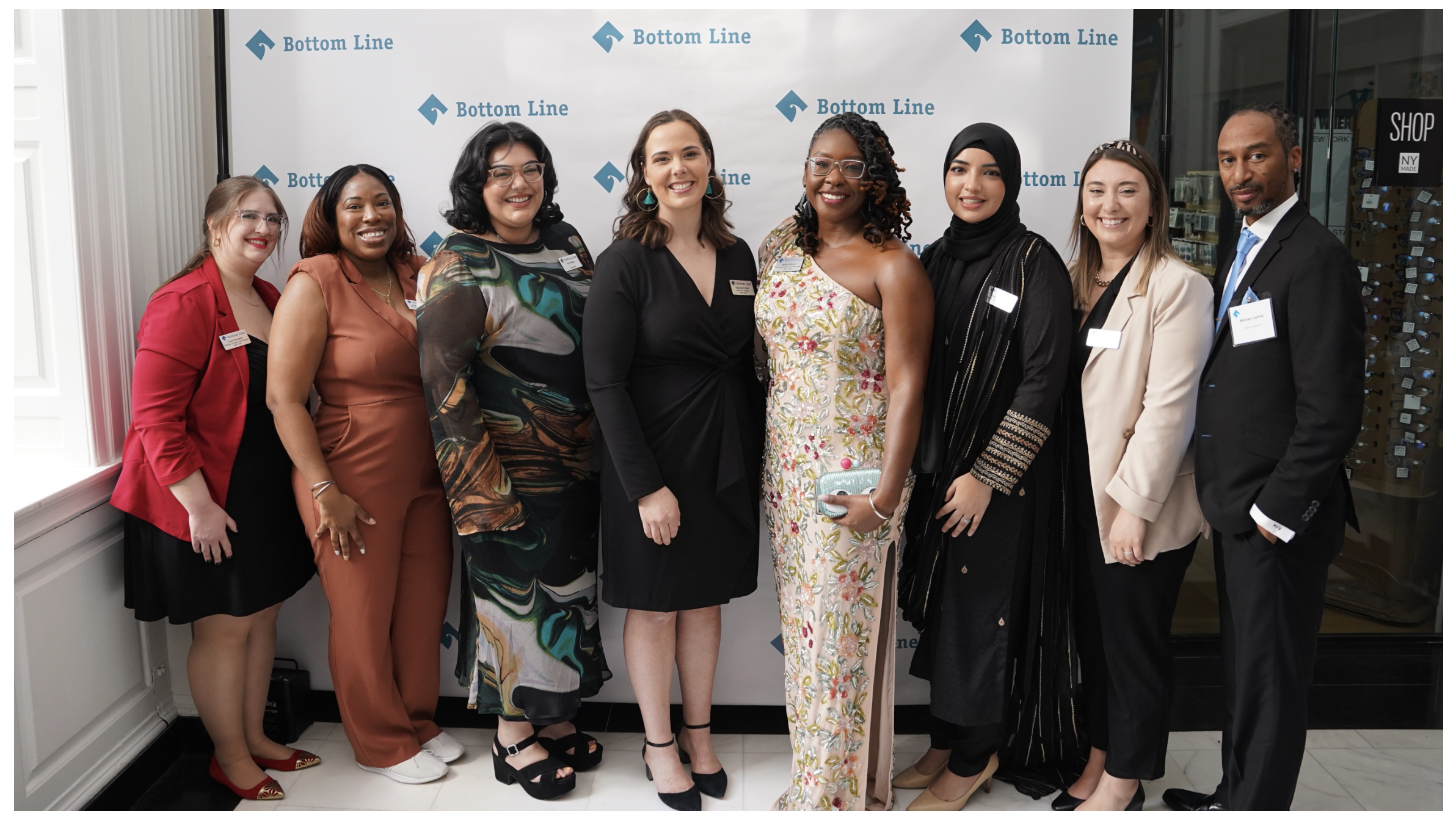 Smiling people lined up in front of a wall with the Bottom Line logo