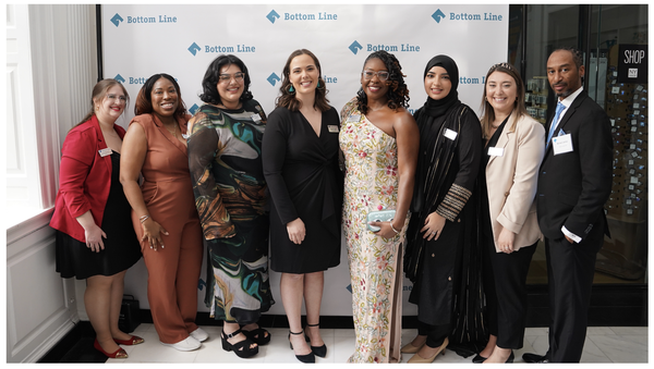 Smiling people lined up in front of a wall with the Bottom Line logo 