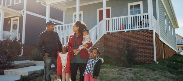 Family smiling with three young children in front of a home